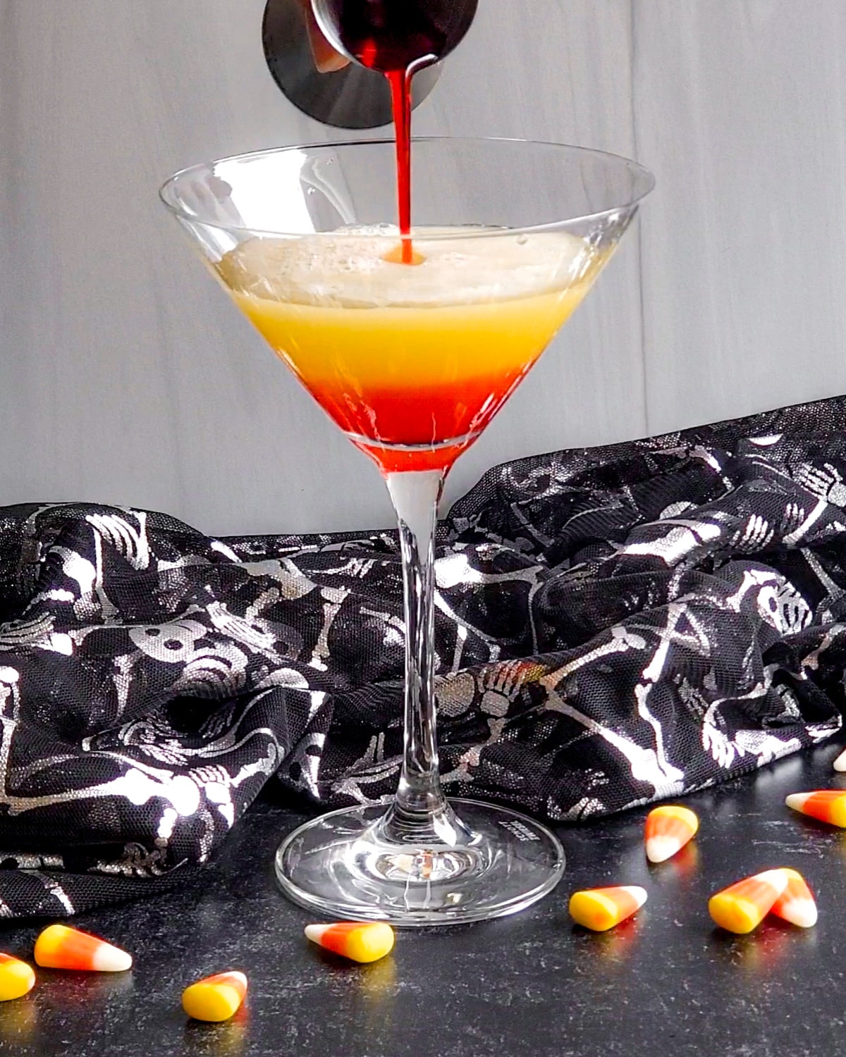 Process shot showing the grenadine being poured over the yellow layer in the martini glass, sinking to the bottom to create the orange layer.