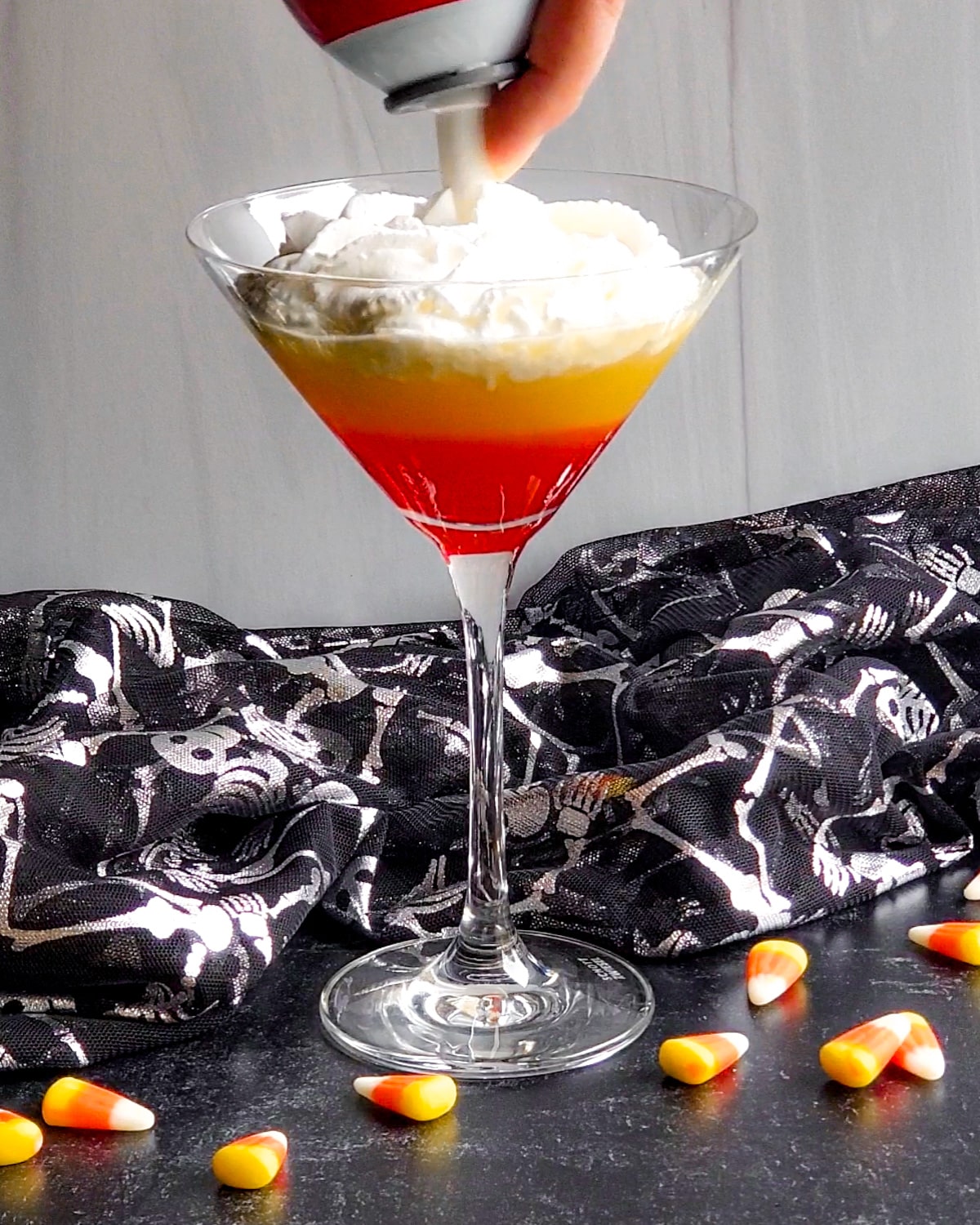 Process shot showing the whipped cream being squirted on top for the white layer in the martini glass.