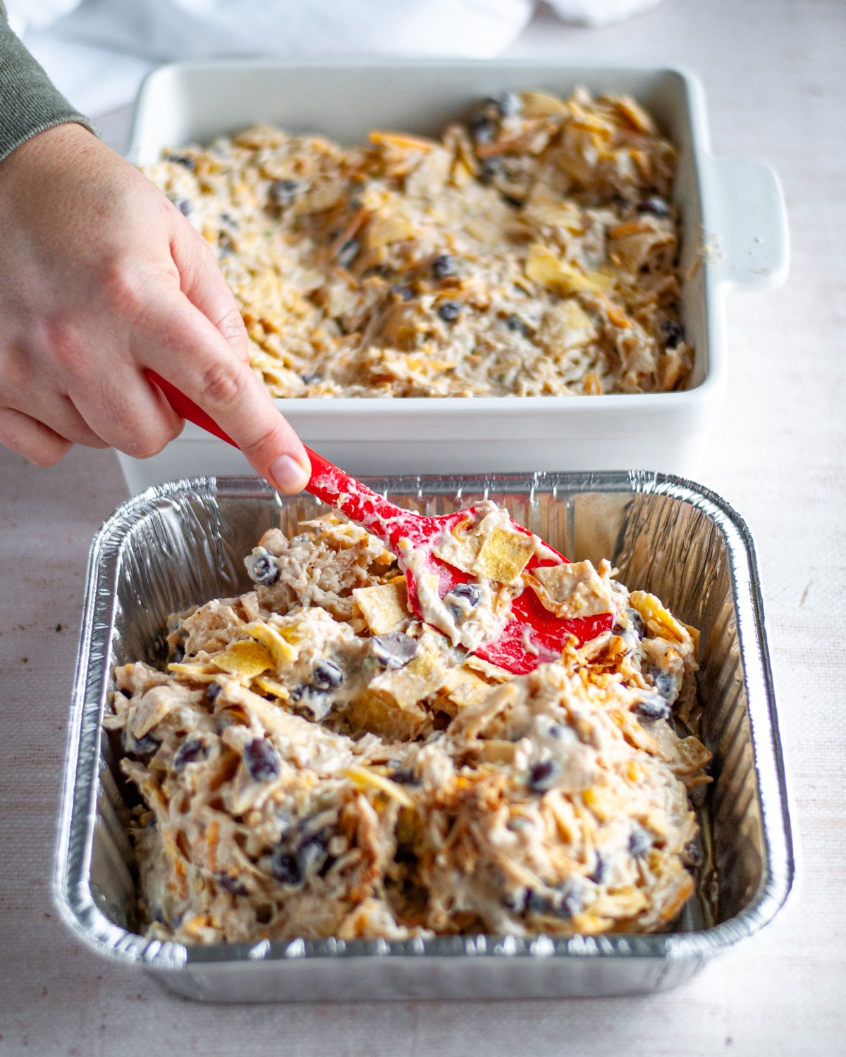 Process shot showing the enchilada casserole filling mixture being pressed into the prepared 8x8 baking dishes.