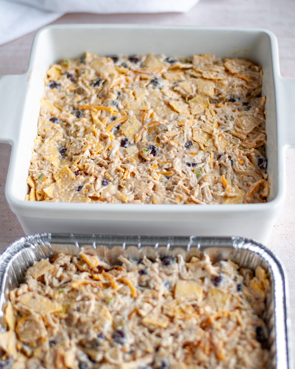 Process shot showing the enchilada casserole filling mixture pressed into even layers in the prepared 8x8 baking dishes.