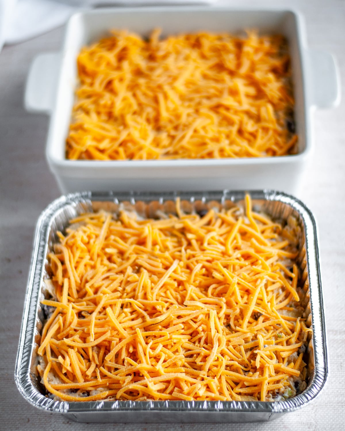 Process shot showing the shredded cheese scatter on top of the two casseroles.
