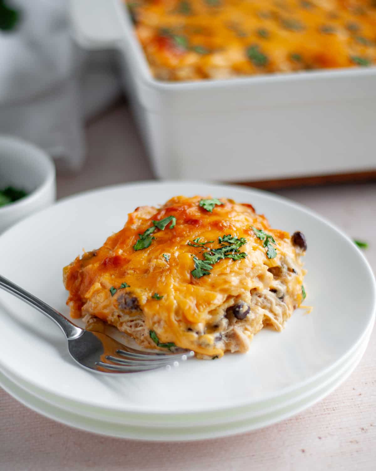 Close up of a slice of chicken enchilada bake on a white serving dish with a fork.