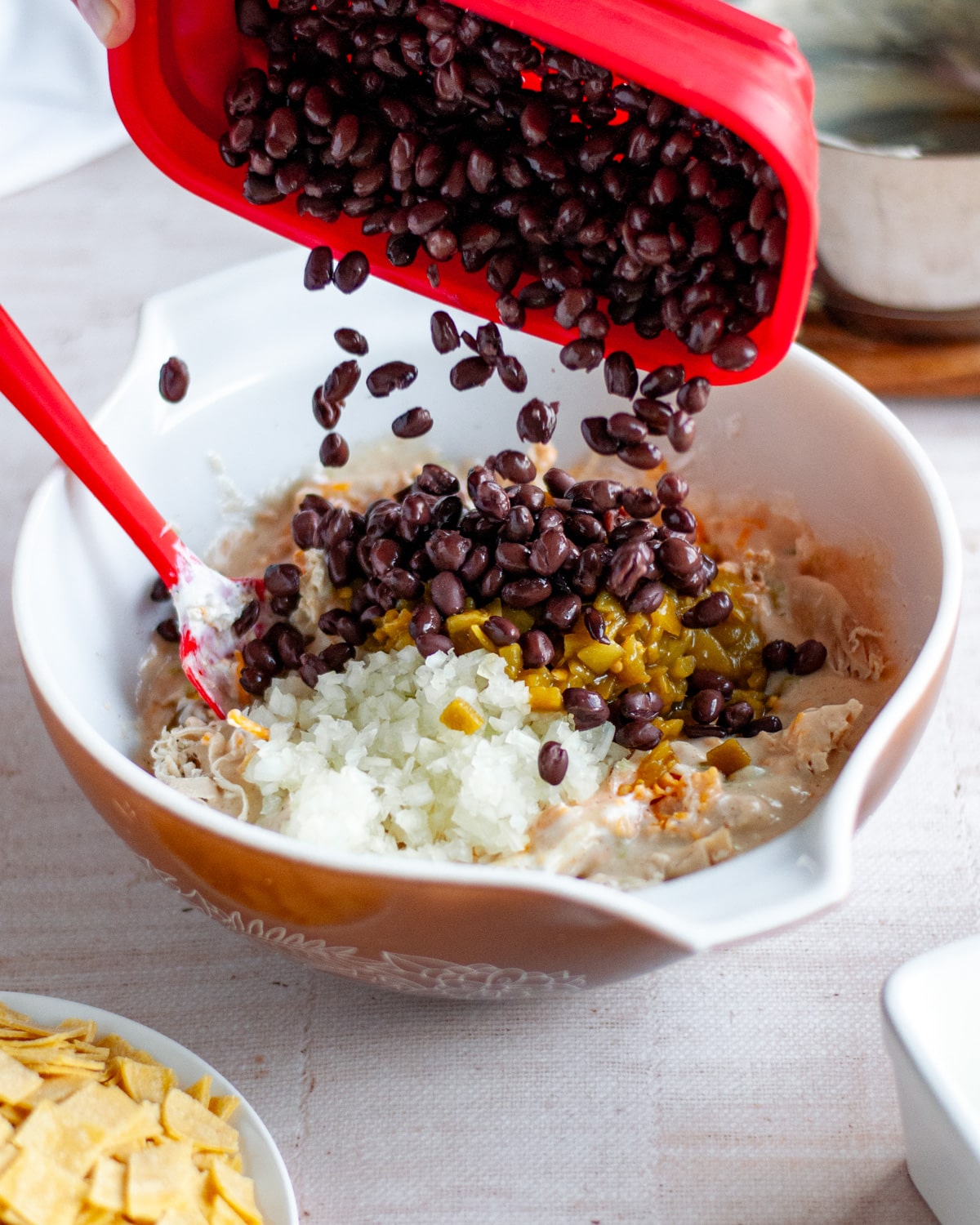 Process shot showing black beans being poured into a large mixing bowl with the other chicken enchilada bake filling ingredients.