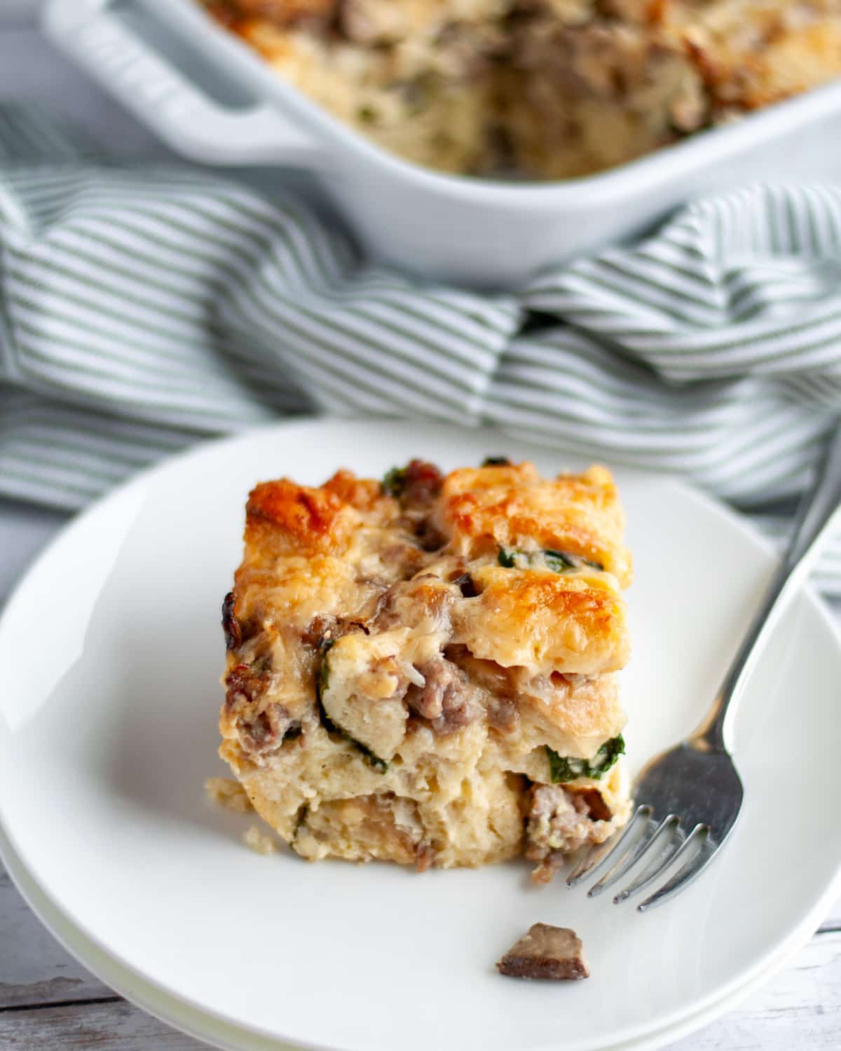 Close up of a slice of baked breakfast casserole with bread on a white serving plate.