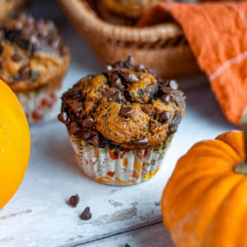 Close up of a swirled double chocolate pumpkin muffin in front of a basket lined with an orange linen and more muffins.