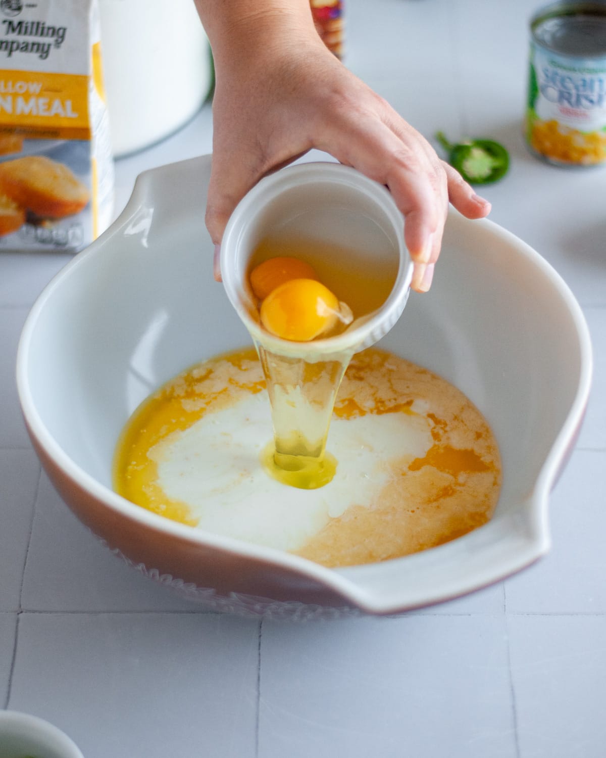 Process shot showing the eggs being added to the other wet ingredients in a large mixing bowl.