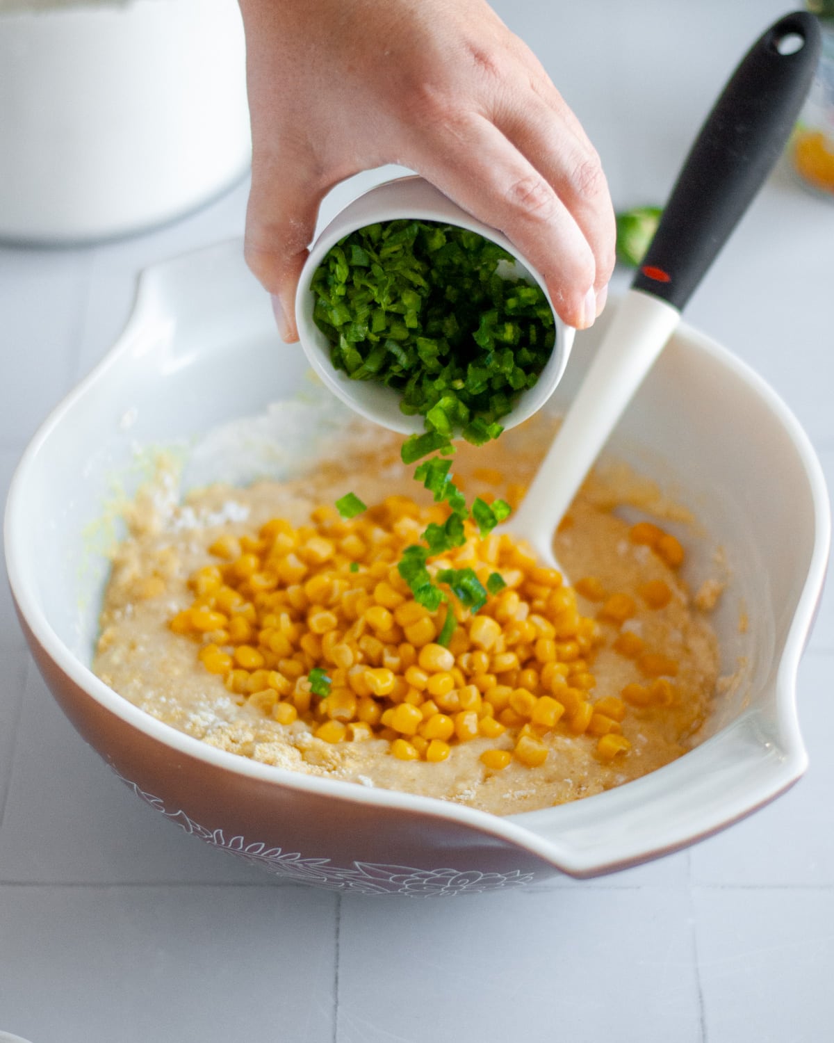 Process shot showing the chopped green onions and jalapenos being poured into the mixing bowl.