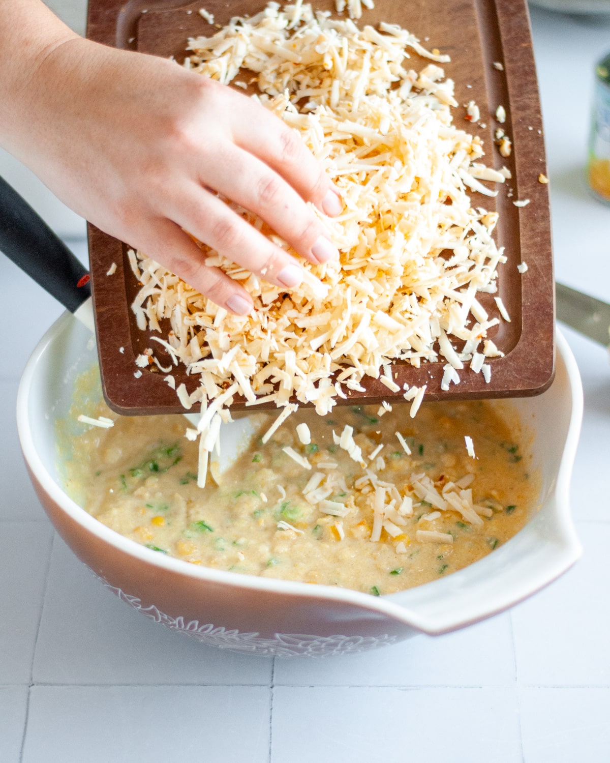 Process shot showing the shredded cheese being added into the mixing bowl.