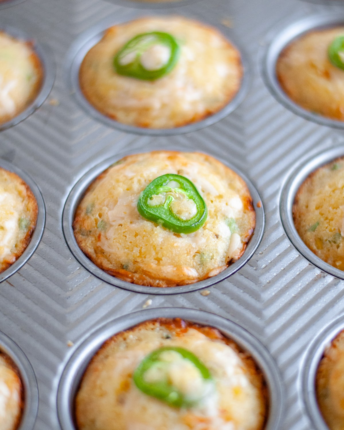 Close up of the baked buttermilk cornbread muffins with jalapenos in the muffin tin, fresh out of the oven.
