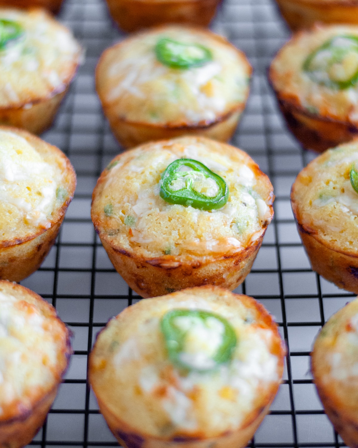 Close up of the baked buttermilk cornbread muffins with jalapenos on a wire cooling rack.
