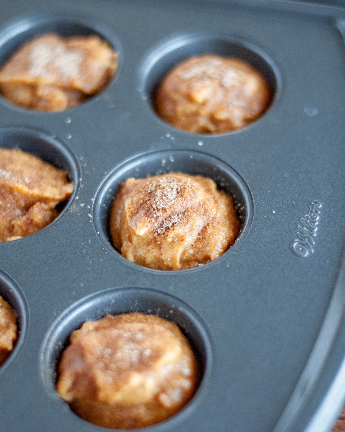 Close up of the cinnamon-sugar topped batter in the muffin tin, ready to go into the oven.