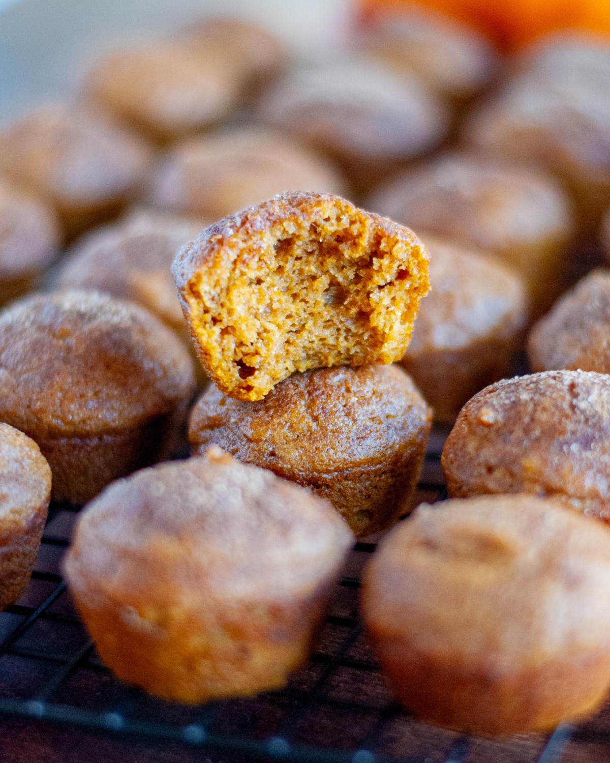 Close up of a pumpkin mini muffin with a bite out of it sitting on top of another muffin on the wire cooling rack.