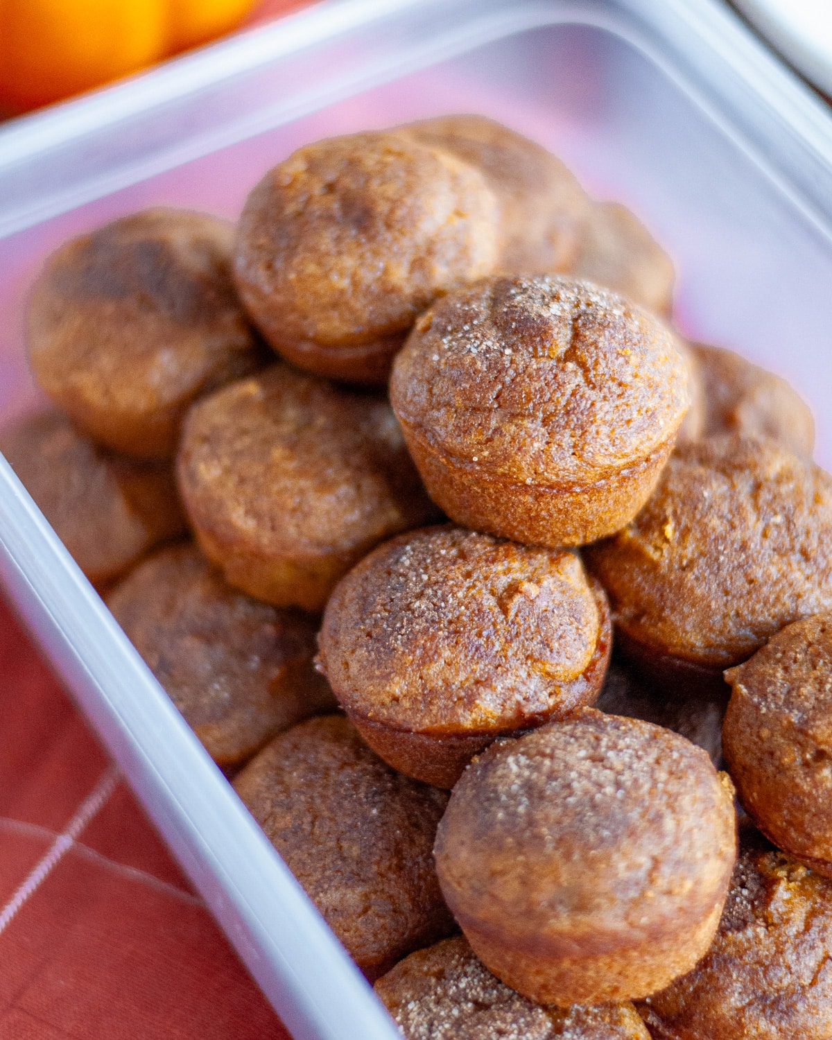 A plastic storage container filled with fully cooled pumpkin mini muffins, ready for storing.