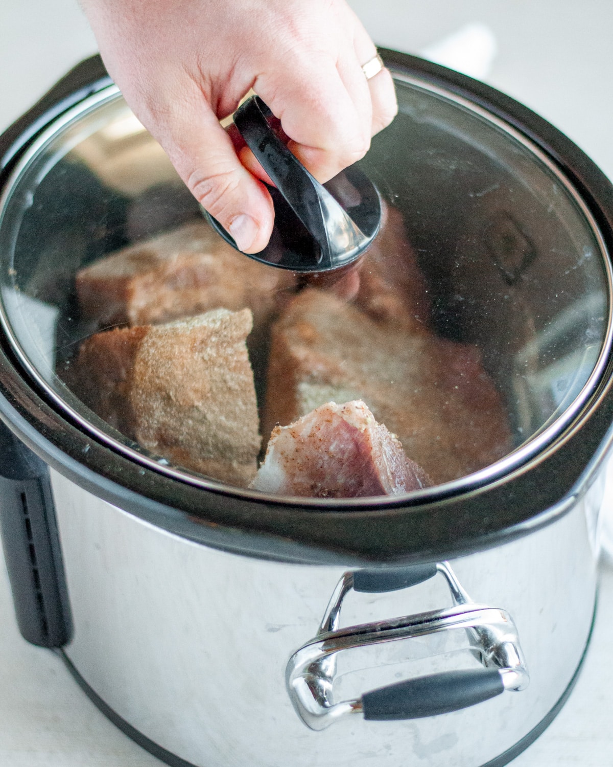 Process shot showing the lid being placed on the slow cooker so the pork can be cooked.