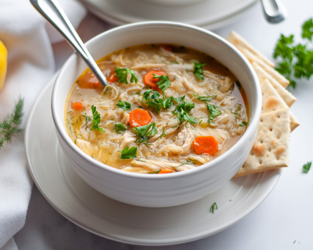 A bowl of lemon chicken and rice soup with a spoon in it and garnished with fresh parsley.