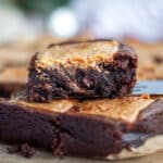 Close up of a peppermint bark brownie sitting on top of a couple of other brownies, showing off the ultra fudgy center.
