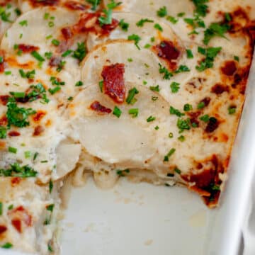 Close up of the pan of loaded scalloped potatoes with a slice taken out of it, showing the layers of potatoes with cheese dripping out.