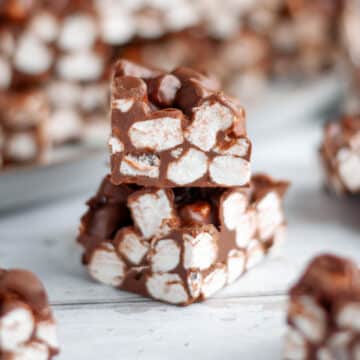 Feature image showing a close up of a stack of two rocky road bars, surrounded by other squares of no bake rocky road.