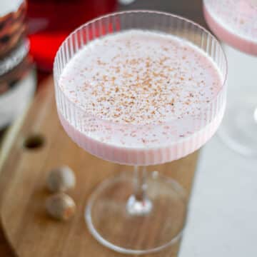 Feature image for our pink squirrel cocktail recipe, showing a vibrant pink drink in a coupe glass topped with freshly grated nutmeg.
