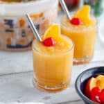 Two low ball glasses filled with Wisconsin brandy slush with a metal straw and garnished with an orange slice and maraschino cherry.