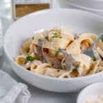 Close up of a bowl of truffled mushroom pasta topped with a sprinkle of chopped parsley and fresh ground black pepper.