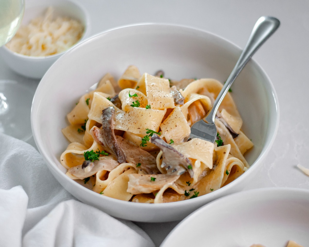 Close up of a bowl of truffled mushroom pasta topped with a sprinkle of chopped parsley and fresh ground black pepper.