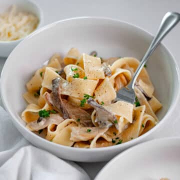 Close up of a bowl of truffled mushroom pasta topped with a sprinkle of chopped parsley and fresh ground black pepper.