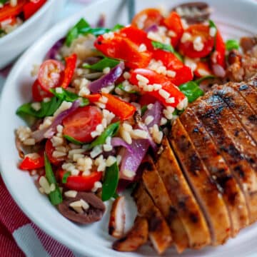 Feature image showing the orzo salad on a serving plate alongside sliced, grilled chicken breast.
