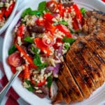 A serving plate filled with mediterranean pasta salad with orzo and a sliced, grilled chicken breast.