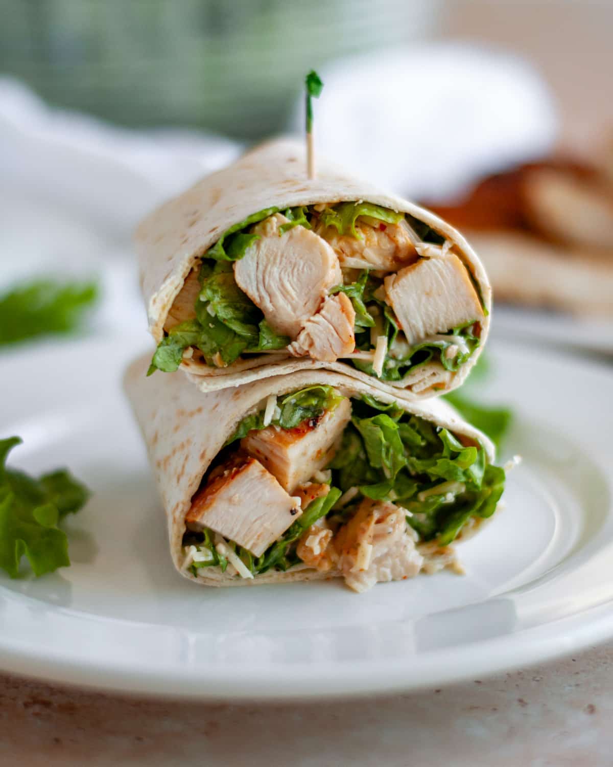 A chicken caesar salad wrap cut in half and stacked on top of each other on a white serving plate with a toothpick stuck into the top wrap.
