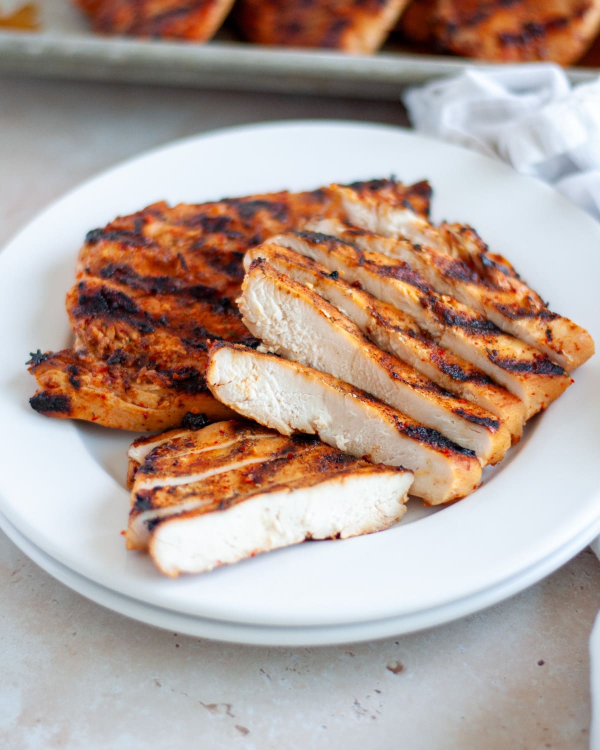 A plate with sliced chicken breast and a full chicken breast to show the juicy inside and deliciously grilled outside.
