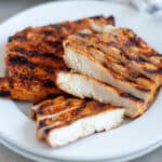 A plate with sliced chicken breast and a full chicken breast to show the juicy inside and deliciously grilled outside.