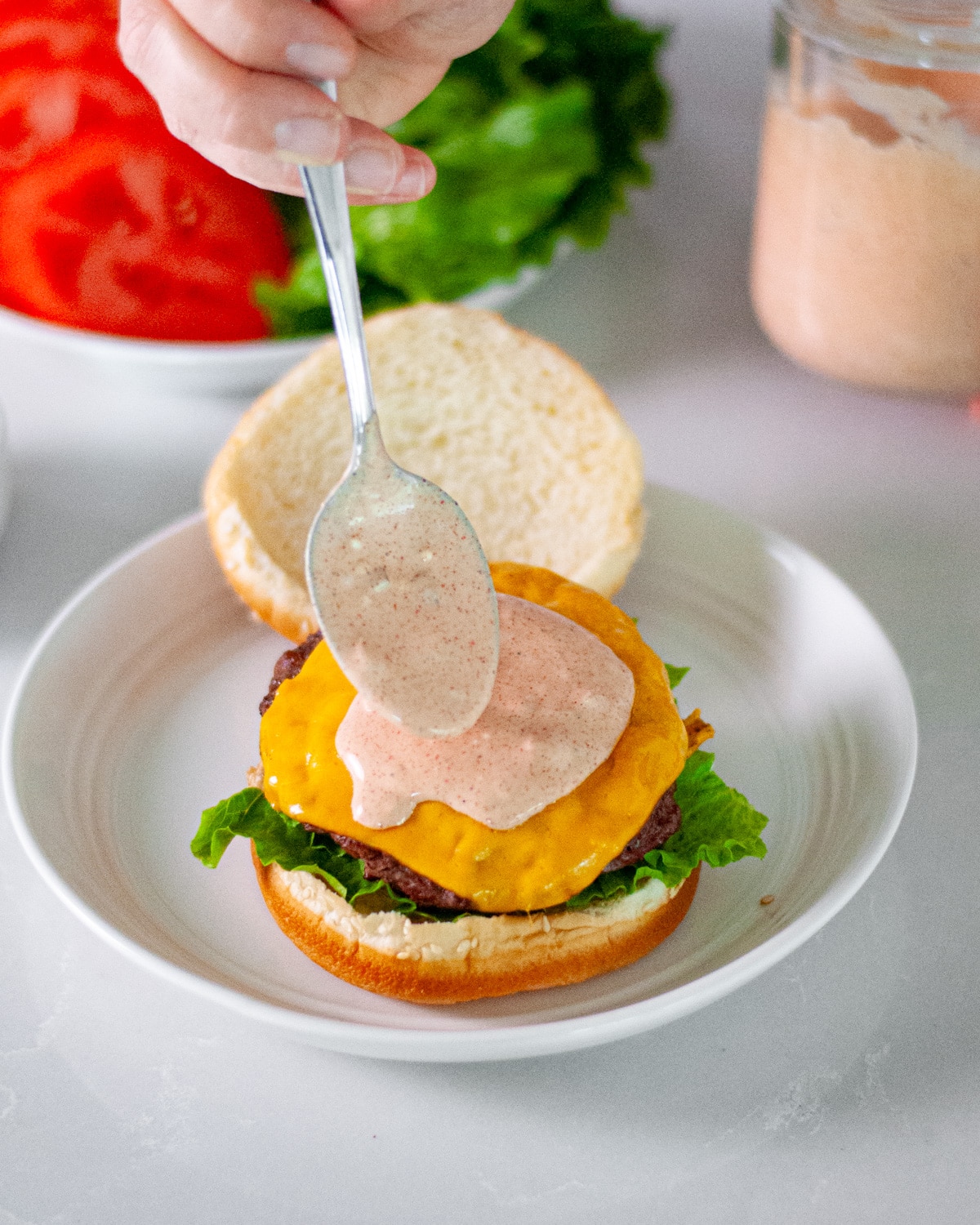 Burger sauce being spooned onto a cheeseburger on a bur.