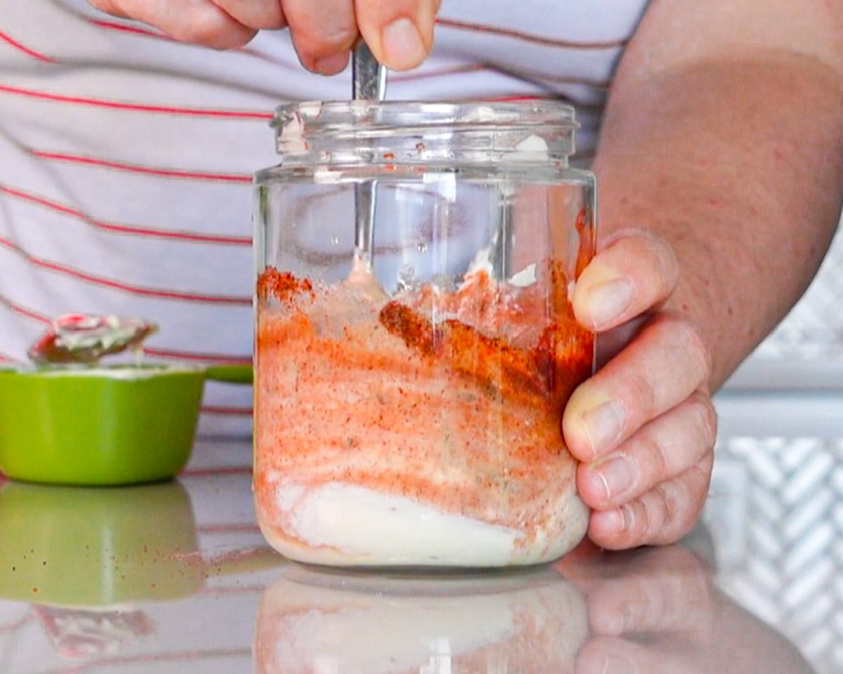 Process shot showing how to make sauce for burgers, showing all the ingredients being stirred together in a jar.