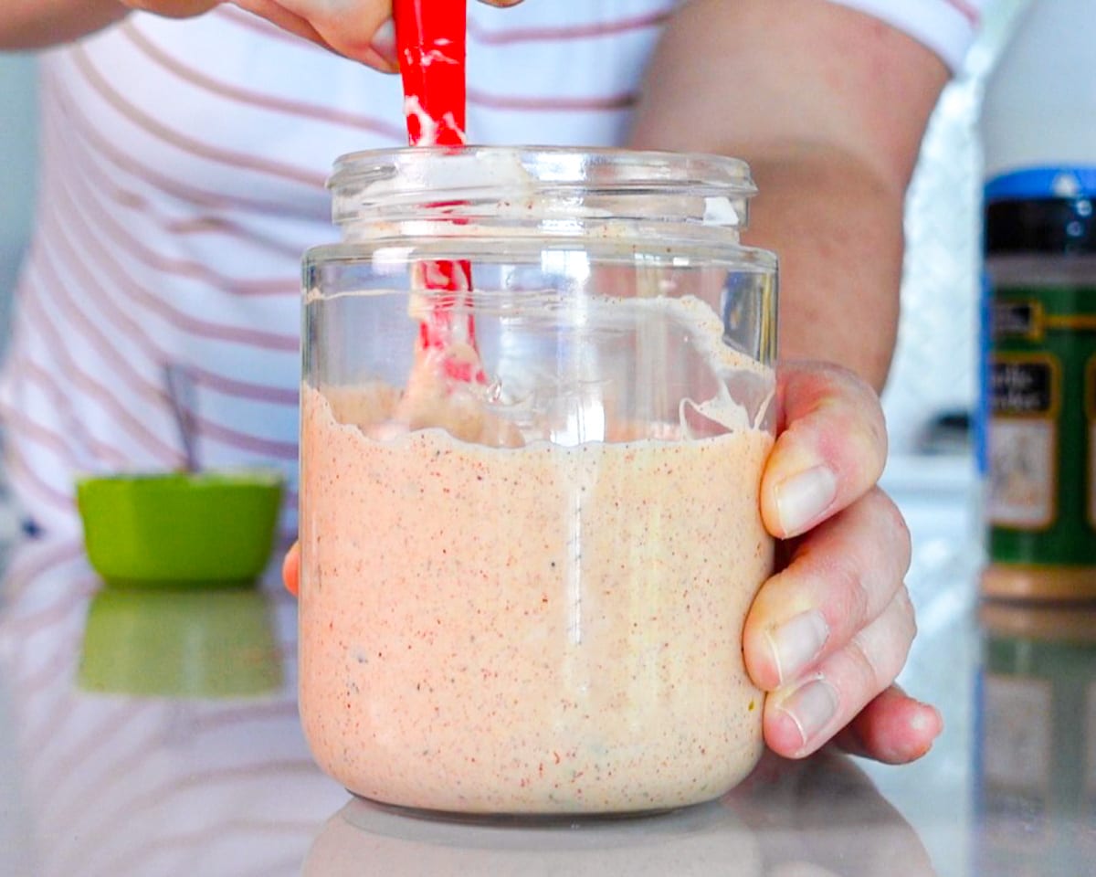 Process shot showing how to make sauce for burgers, showing all the ingredients being stirred together in a jar.