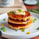 Feature image showing a stack of three corn fritters topped with additional spreadable cheese, slices of green onion, and a drizzle of hot honey.