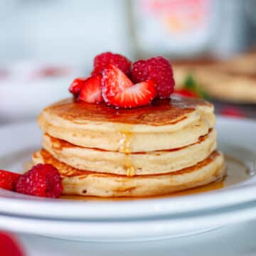 Feature image showing a stack of 3 cottage cheese pancakes topped with berries and maple syrup dripping down the side of the stack.