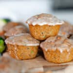 Feature image showing a close up side profile of 3 glazed carrot & zucchini muffins stacked on a wooden board.