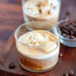 Close up of a freshly made affogato on a wooden tray with espresso beans around it and another affogato in the background.