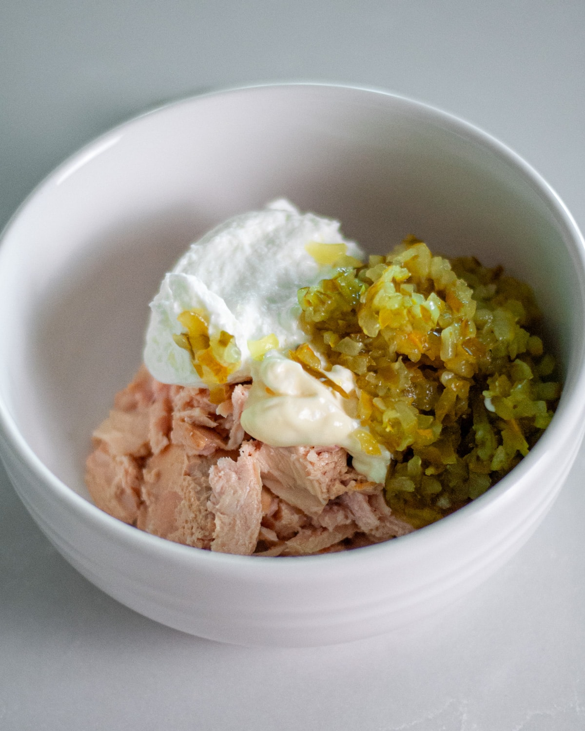Process shot showing the flakey canned tuna, yogurt, mayo, and pickle relish in a bowl.