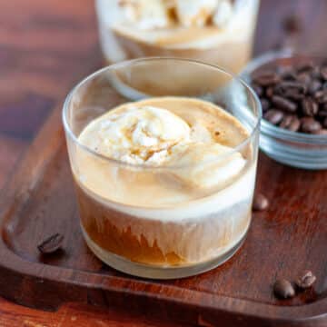 Close up of a freshly made affogato on a wooden tray with espresso beans around it and another affogato in the background.