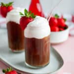 A close of up a tall cold brew coffee topped with a generous portion of strawberry cold foam, a strawberry for garnish, and a straw.