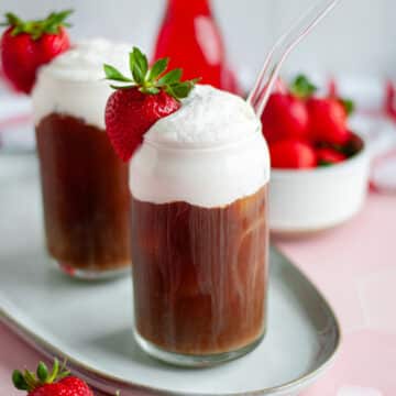 A close of up a tall cold brew coffee topped with a generous portion of strawberry cold foam, a strawberry for garnish, and a straw.
