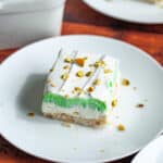 A square of the layered pistachio pudding dessert on a white serving plate, topped with chopped pistachios.