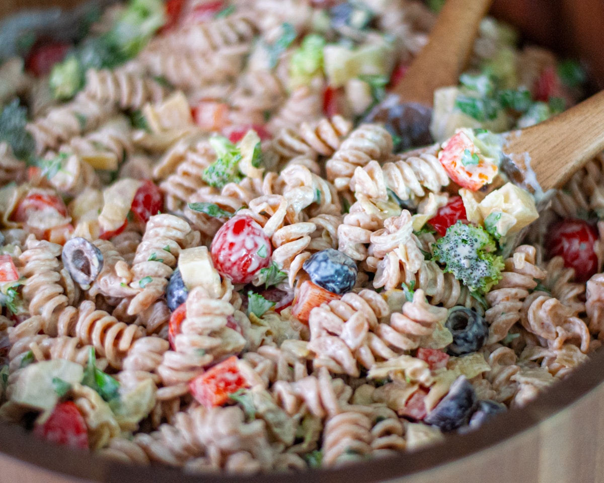Close up of the creamy pasta salad with cottage cheese dressing in a large wooden serving bowl with wooden serving spoons.