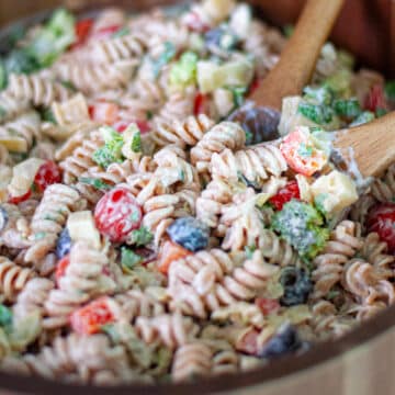 Close up of the creamy pasta salad with cottage cheese dressing in a large wooden serving bowl with wooden serving spoons.