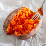 Feature image showing a fork fluffing the cooked inside of a sweet potato, showing the fork-tender and perfectly cooked interior.