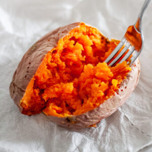 Feature image showing a fork fluffing the cooked inside of a sweet potato, showing the fork-tender and perfectly cooked interior.