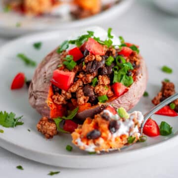 Feature image for our turkey taco stuffed sweet potatoes, showing a medium sweet potato loaded with a turkey and black bean taco filling and all kinds of delicious taco toppings.