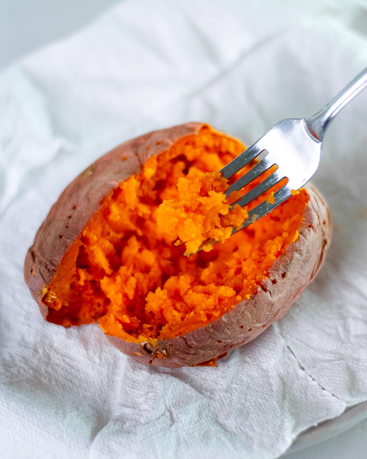 A fork showing off a scoop of the fluffed interior or a microwave sweet potato, showing that it's fork-tender and perfectly cooked inside.